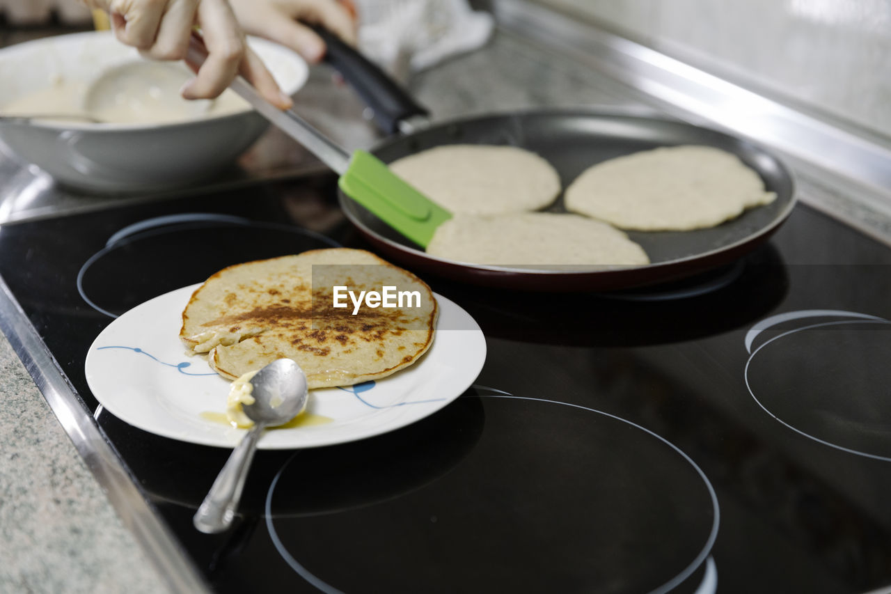 Anonymous person using spatula to turn pancakes on pan cooking pastry person