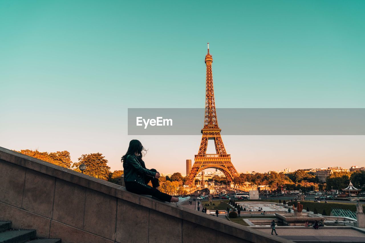 Woman sitting against eiffel tower in city