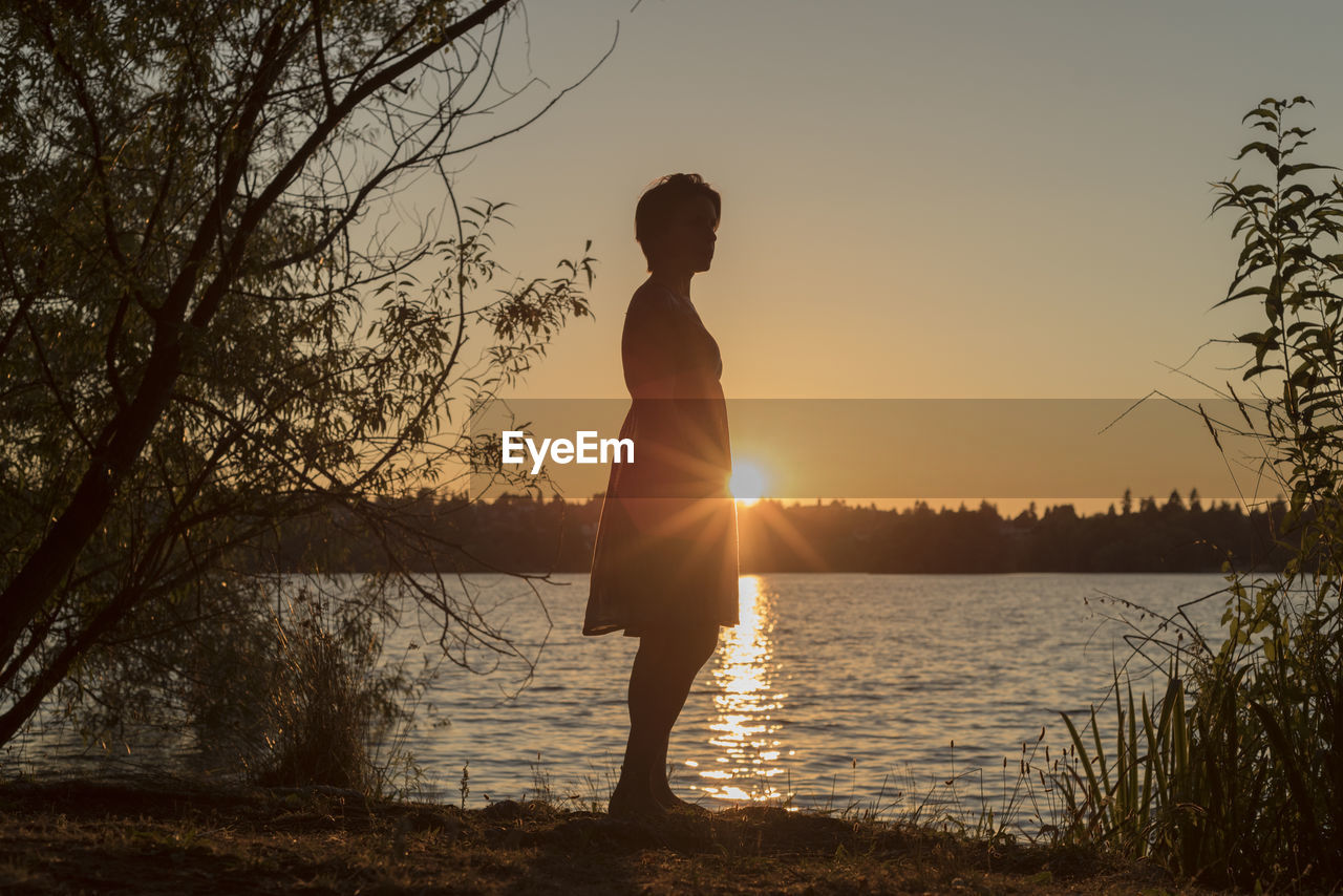 SILHOUETTE MAN WITH SUN SHINING OVER LAKE DURING SUNSET