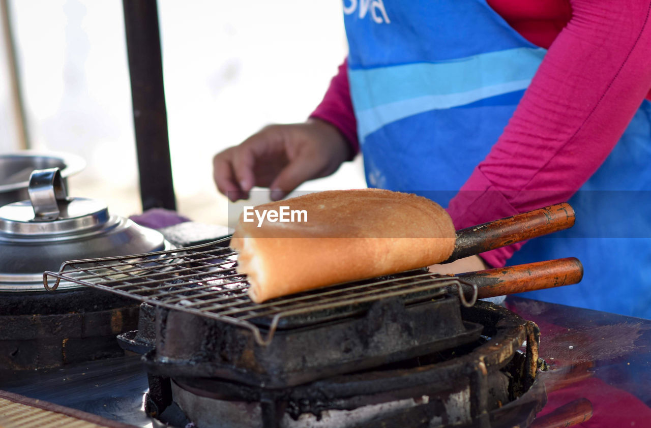 CLOSE-UP OF PERSON PREPARING FOOD ON BARBECUE GRILL