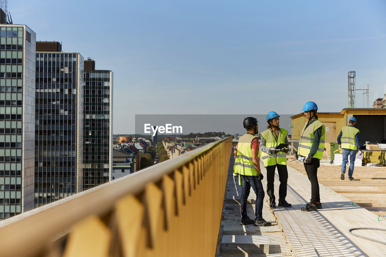 Female and male engineers discussing at construction site against sky