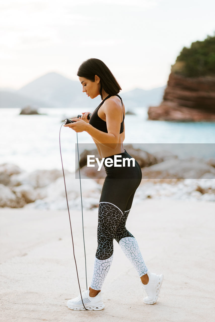 Side view of woman skipping rope at beach