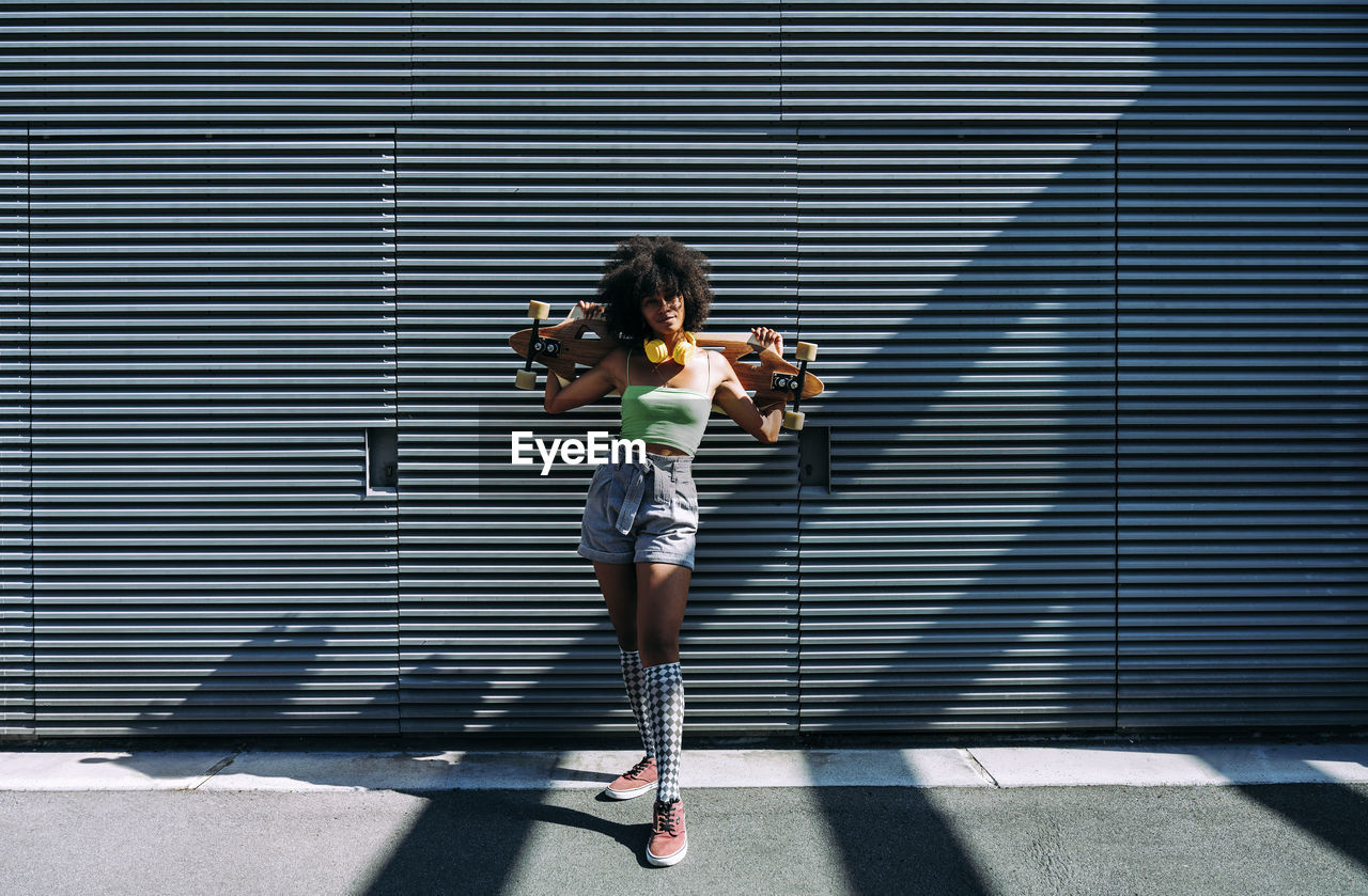 Woman with skateboard standing in front of wall