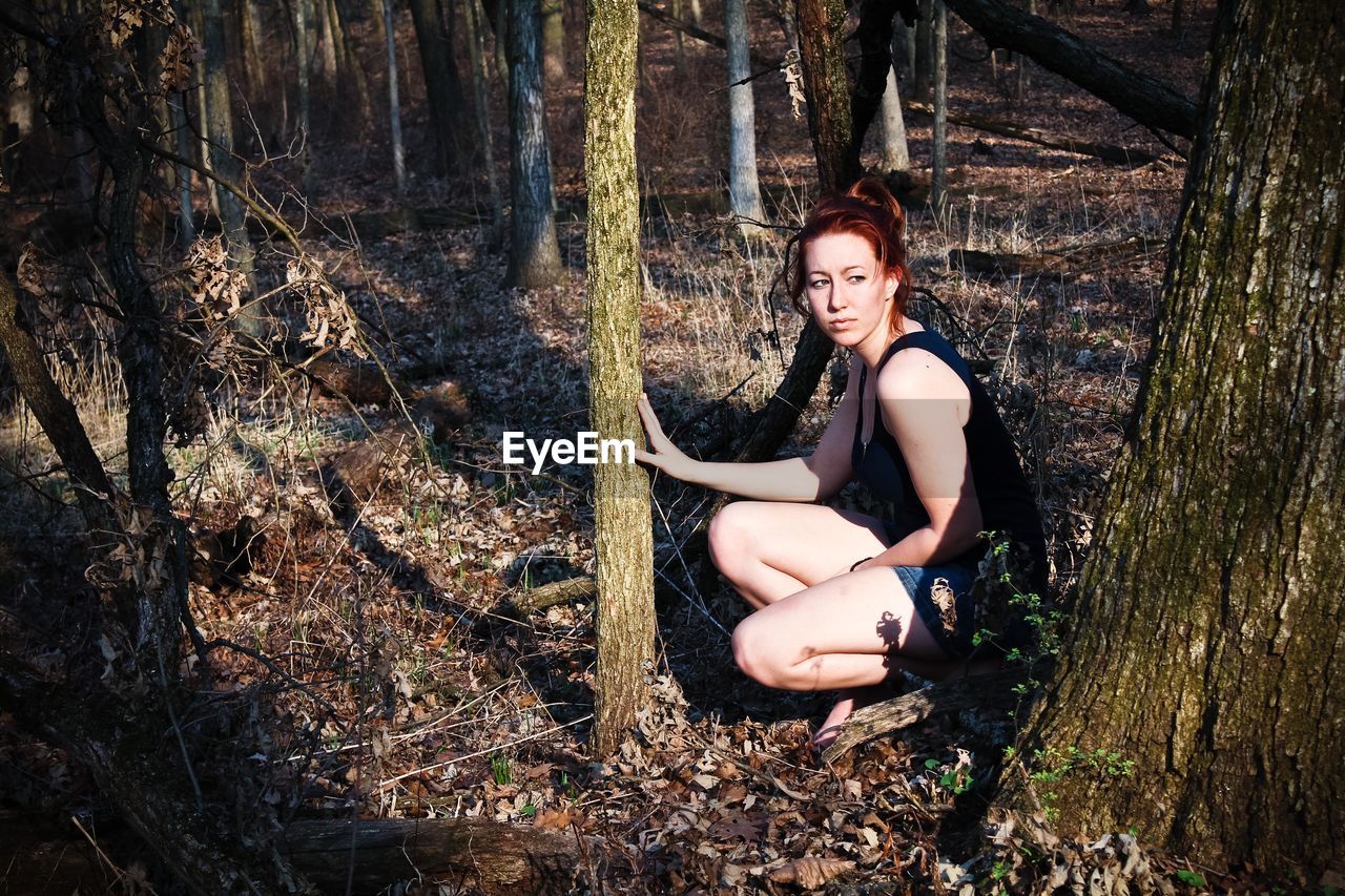 Young woman crouching against trees at forest