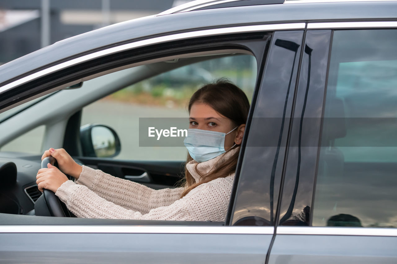 Portrait of woman wearing mask seen through car window