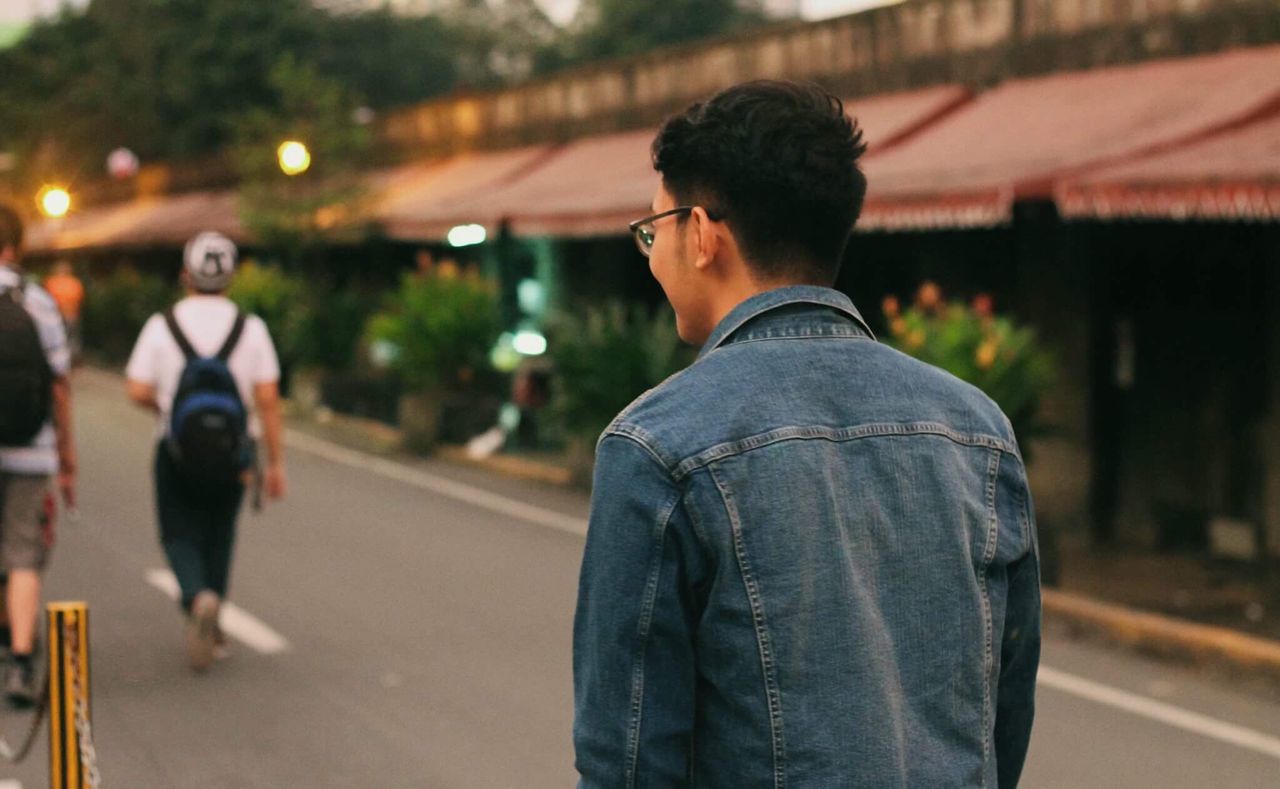 REAR VIEW OF YOUNG MAN WITH ROAD ON THE BACKGROUND