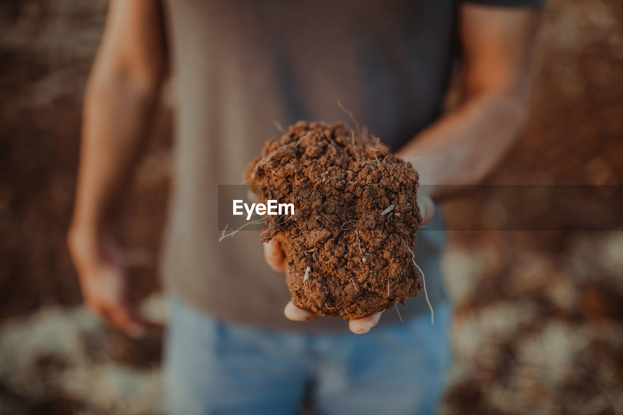 Midsection of man holding soil while standing on field