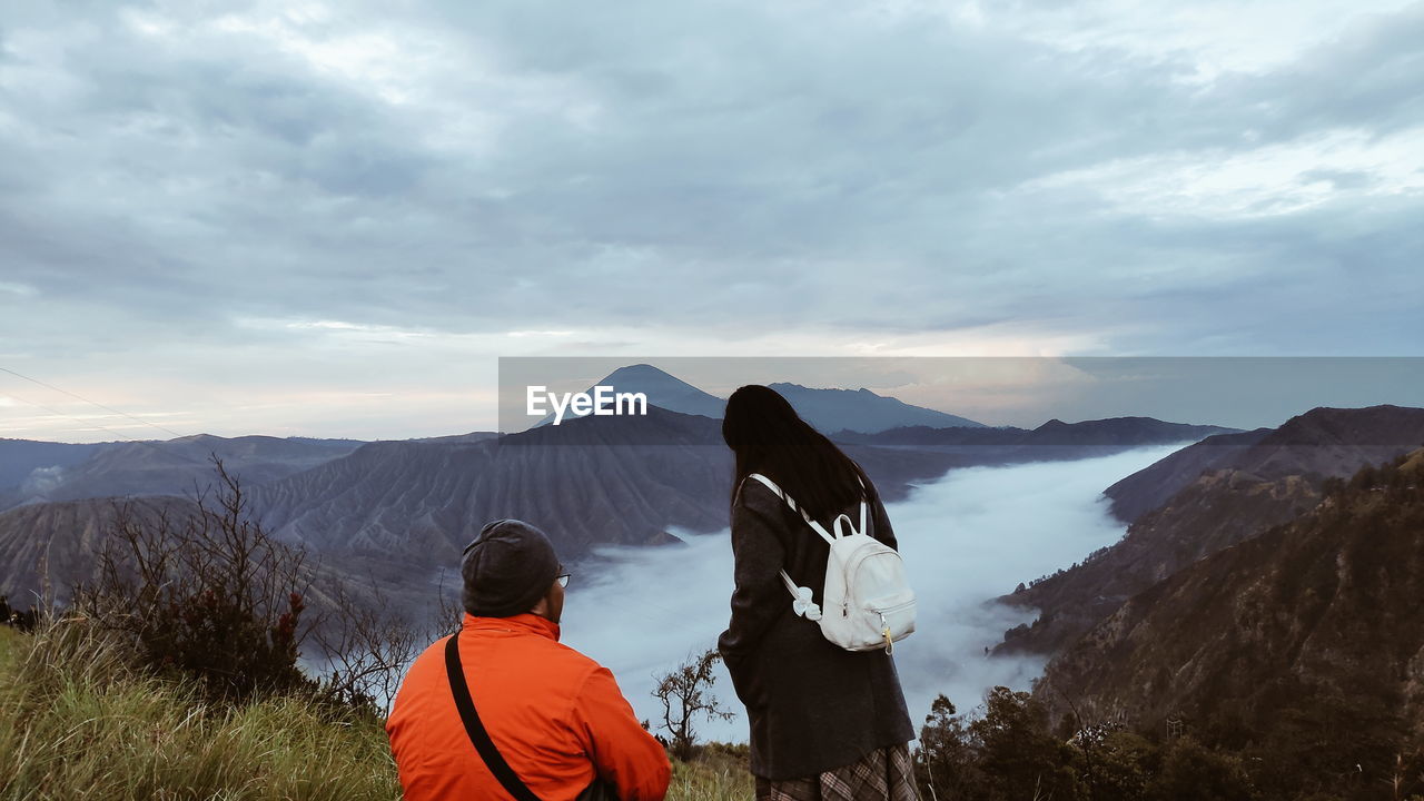 Rear view of people looking at mountains against sky