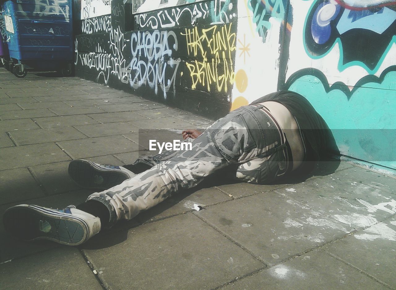 Men lying on sidewalk against graffiti wall
