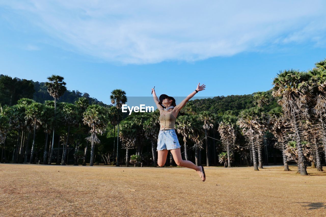 FULL LENGTH OF HAPPY WOMAN JUMPING AGAINST TREES