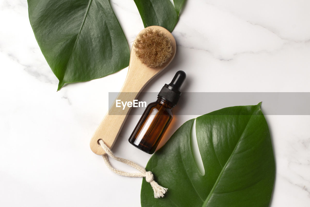 Cosmetic serum in brown glass bottle and body brush on a marble background with monstera palm 