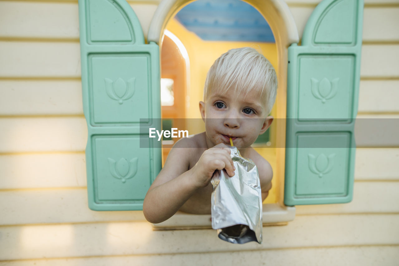 Close-up of boy having drink while looking through window in playhouse