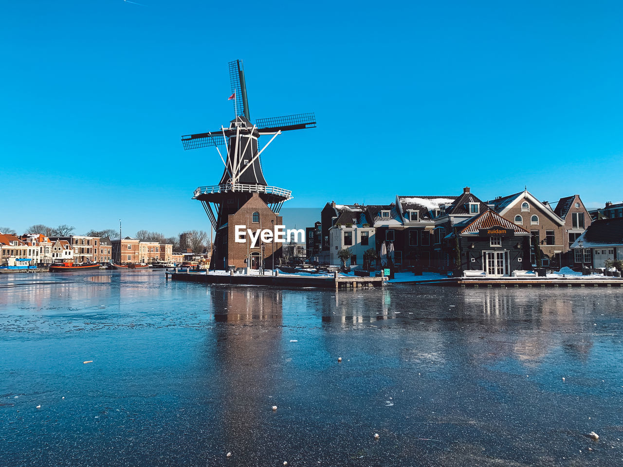 Buildings by river against clear blue sky