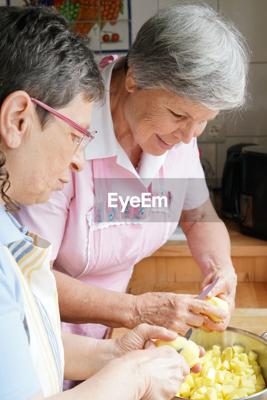 Senior women cutting potatoes in kitchen home