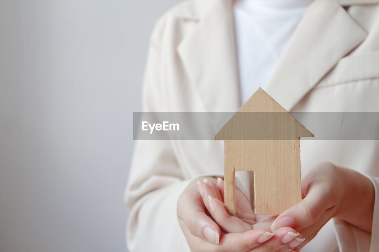 Woman hand holding miniature wood house or model of home, choosing the right real estate property.