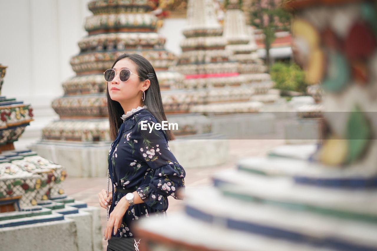 Woman wearing sunglasses looking away while standing by built structure