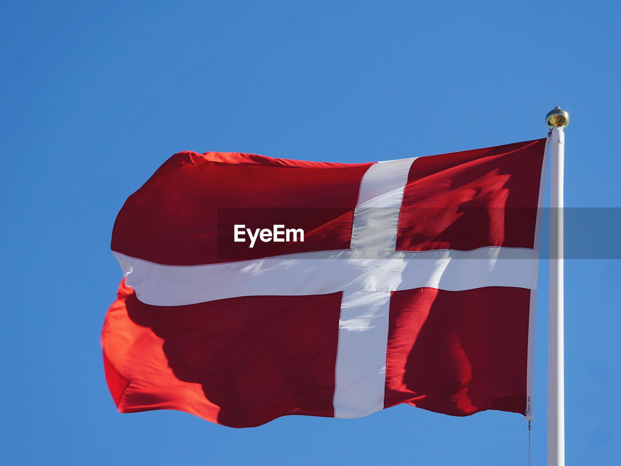 Low angle view of danish flag waving against clear blue sky