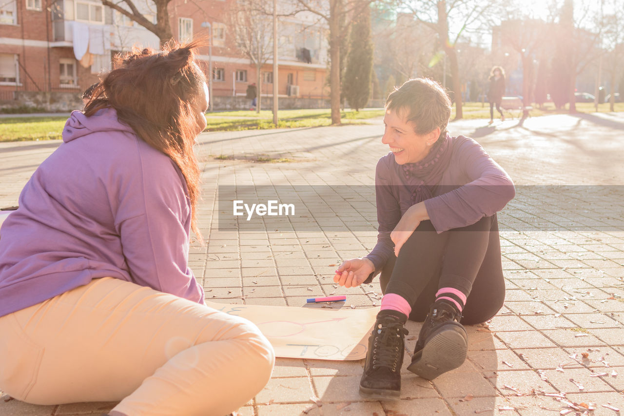 Smiling women with poster sitting on street