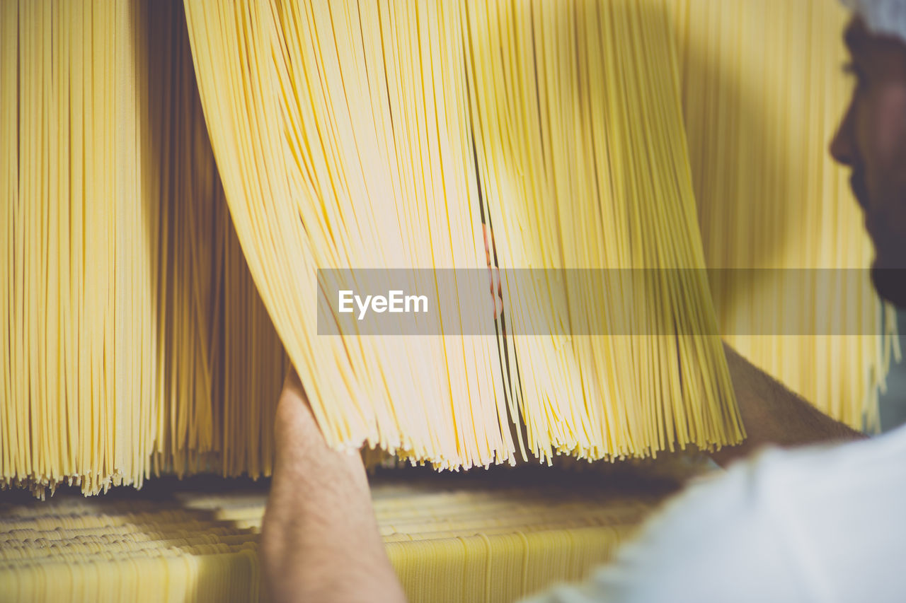 Cropped image of person checking spaghetti drying in factory