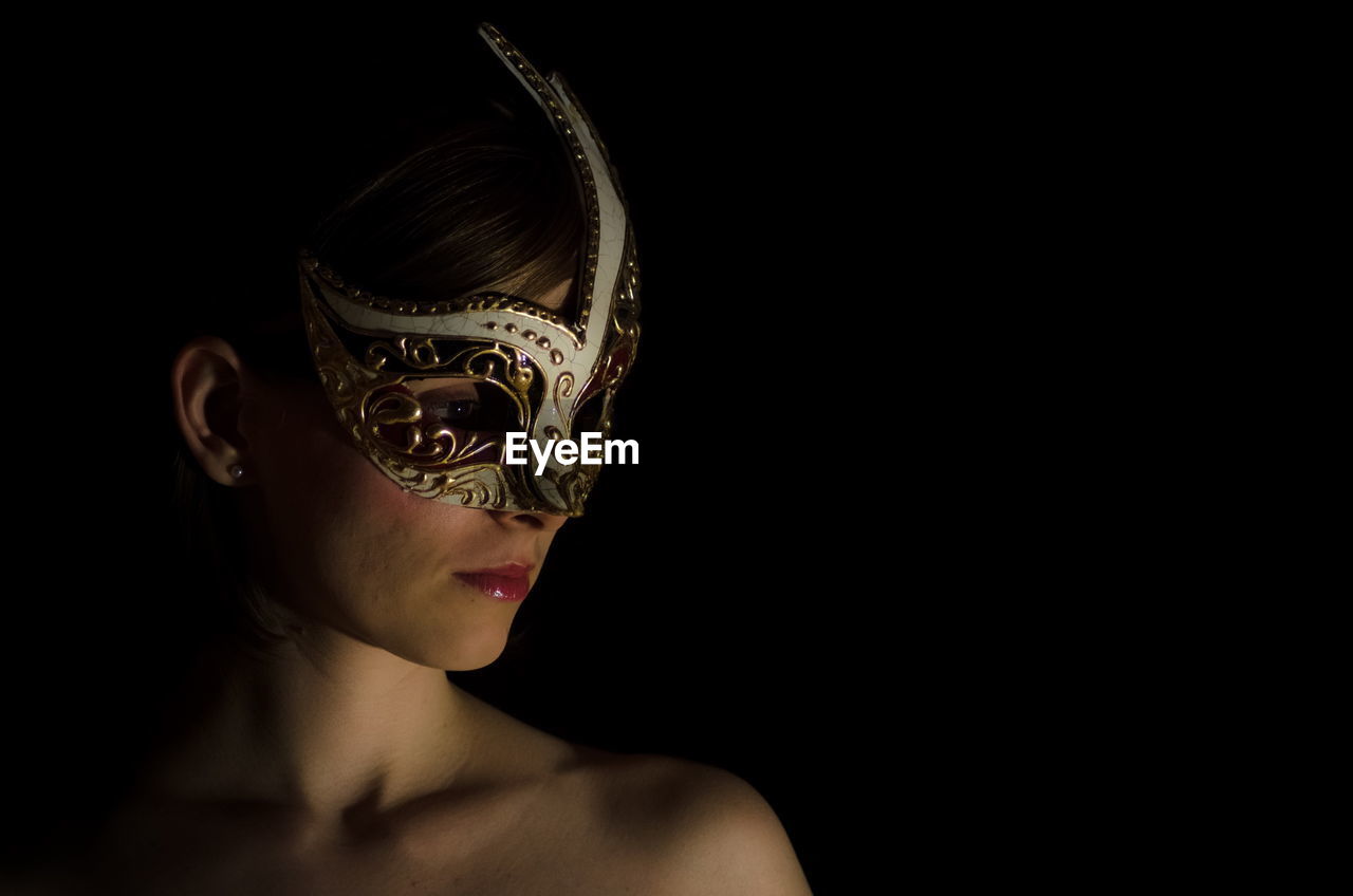 Topless woman wearing carnival mask against black background