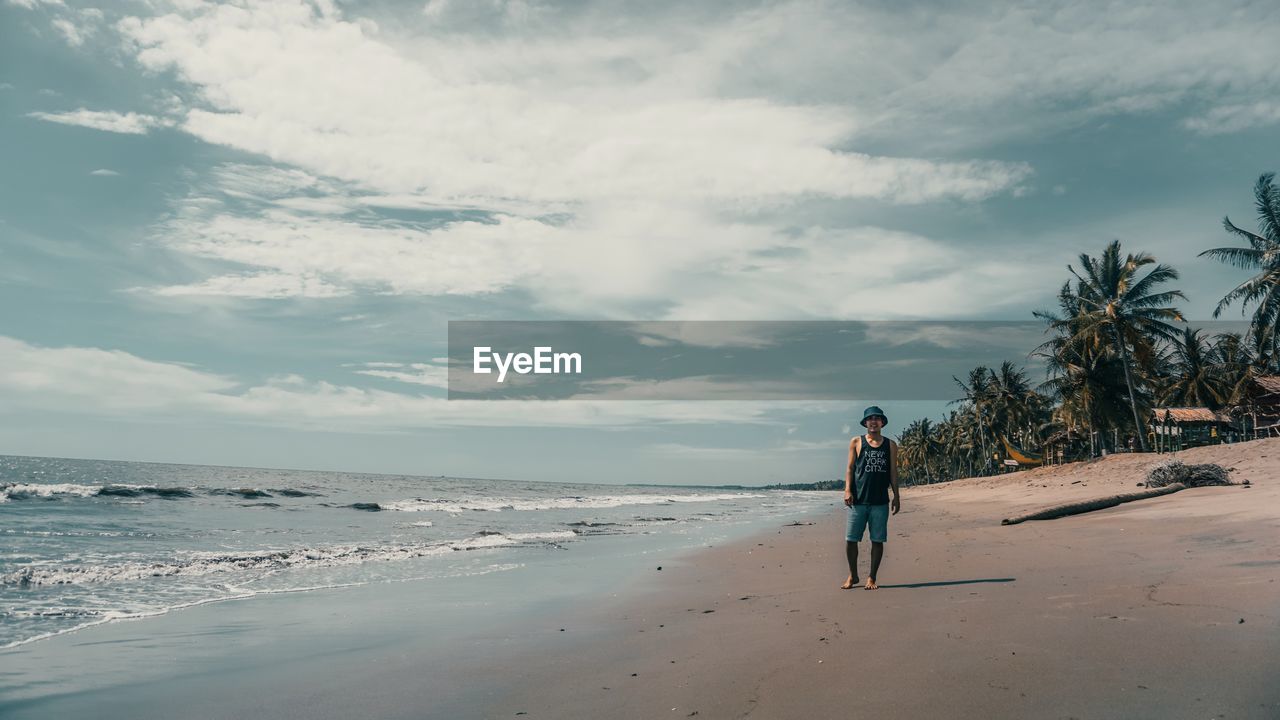 MAN WALKING ON BEACH AGAINST SEA