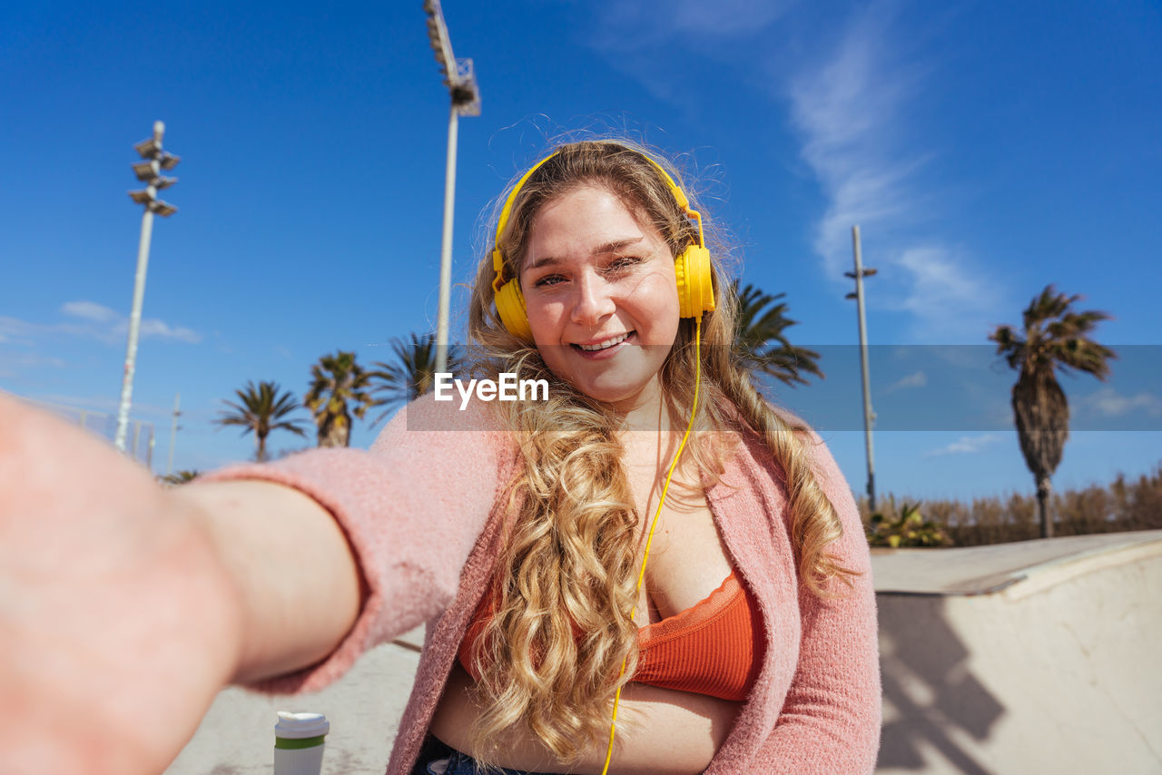 Portrait of smiling woman taking selfie against sky