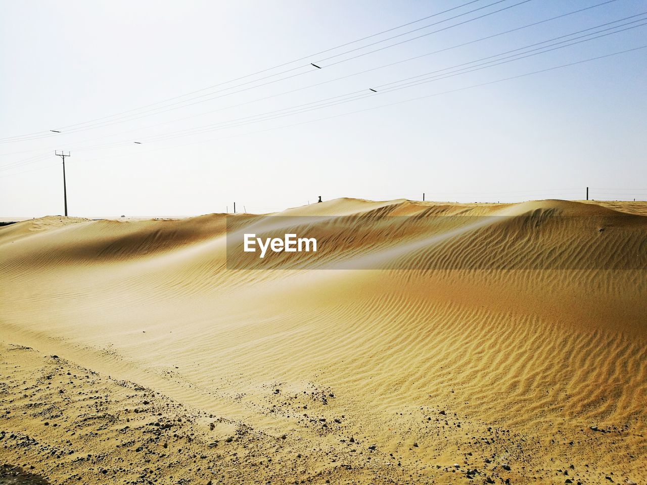 Low angle view of electricity pylon on sand against sky during sunny day