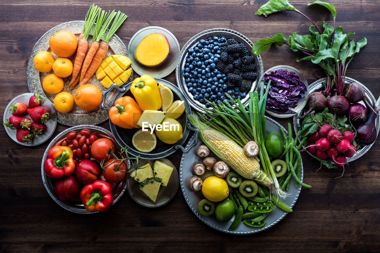 Various fresh organic fruits and vegetables in rainbow colours against a dark wooden background.