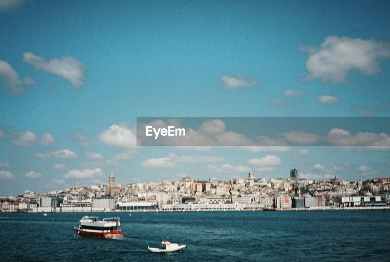 Sailboats in sea by buildings in city against sky