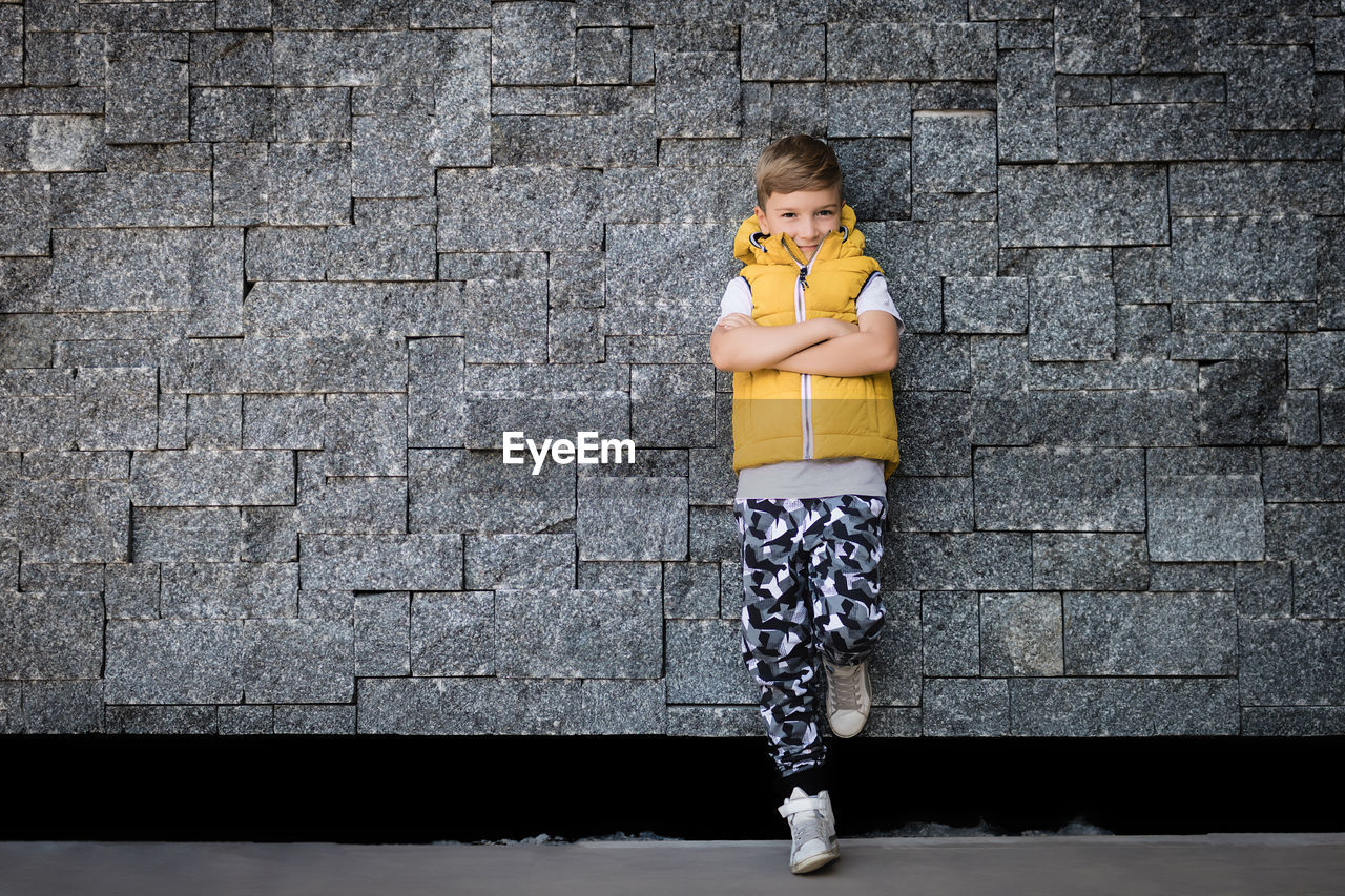 Smiling boy with arms crossed leaning on brick wall and looking at camera. copy space.