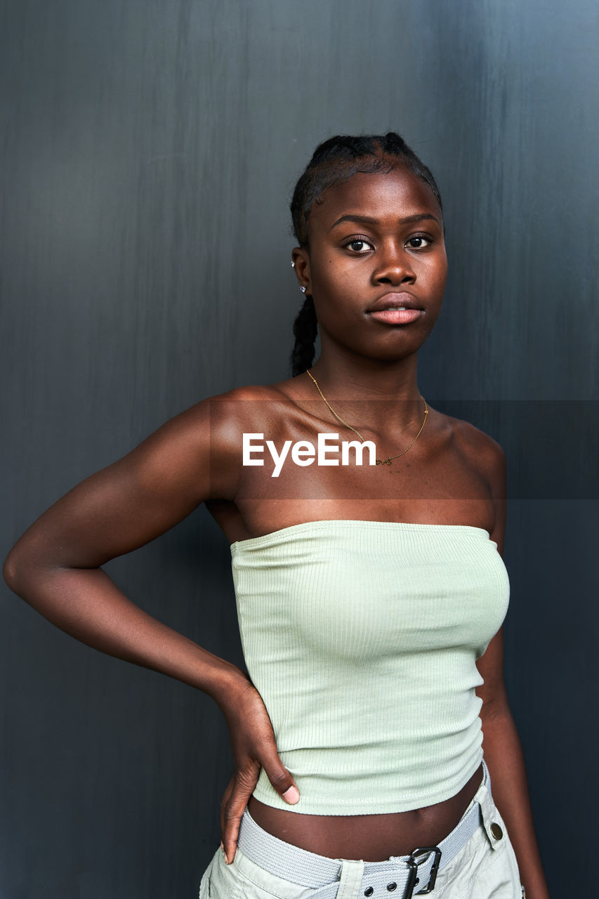 Self assured young african american female with long braids wearing tube top and looking at camera on gray background