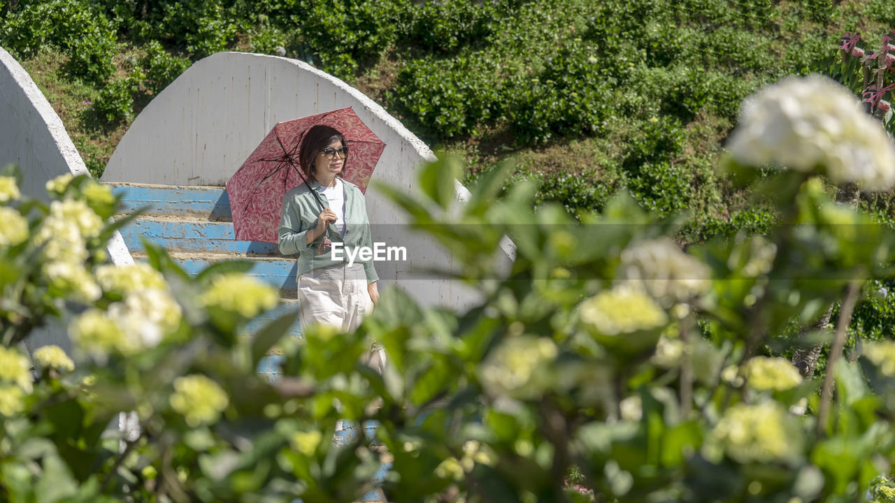 Woman holding umbrella standing by plants
