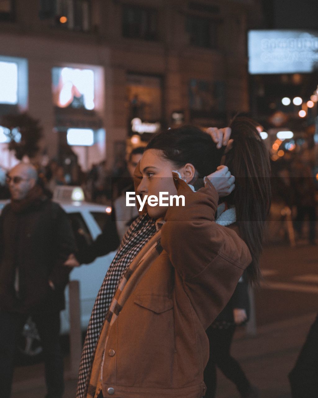 Close-up of woman tying hair in city at night