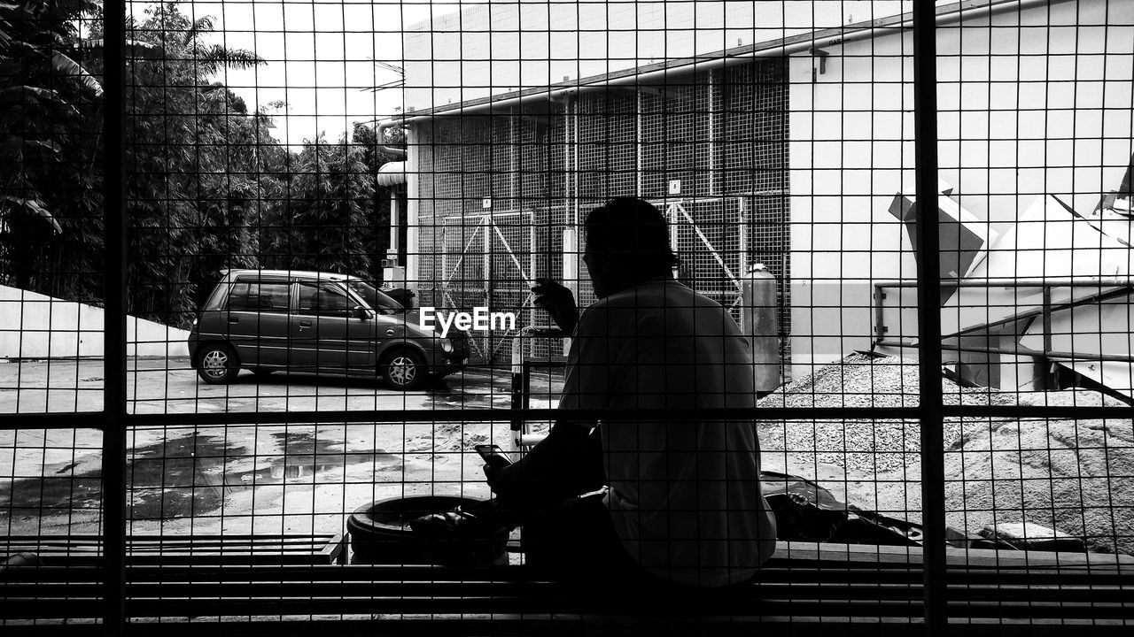 Rear view of man sitting on window sill against house