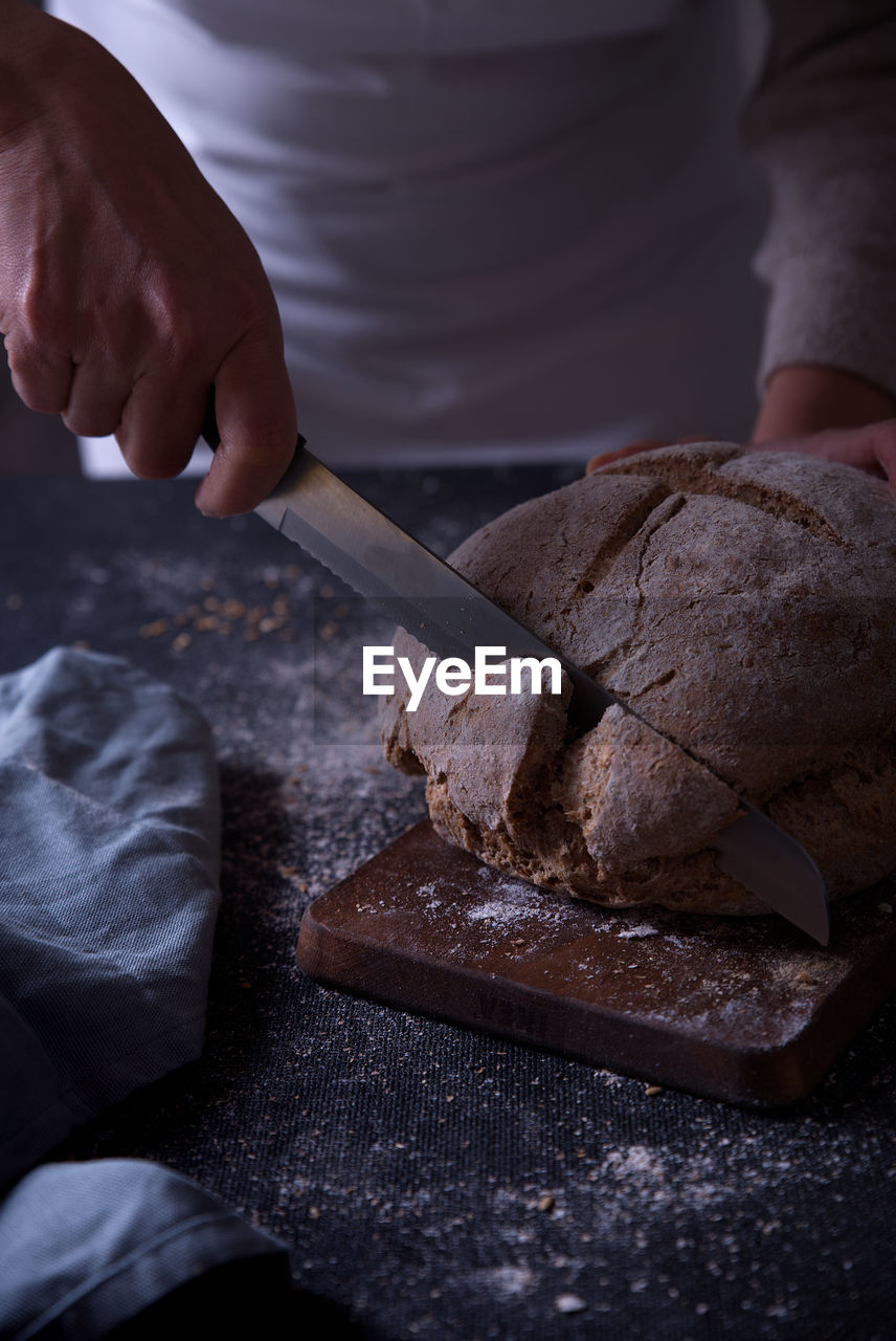 Hands slicing fresh bread, on dark background.