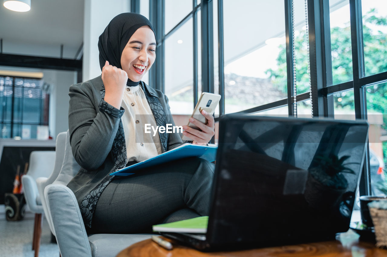 portrait of young woman using laptop while sitting on sofa at home