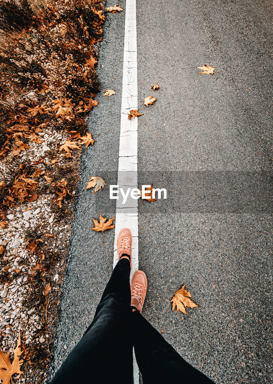 high angle view, low section, autumn, human leg, road, one person, day, leaf, street, plant part, transportation, city, asphalt, personal perspective, nature, marking, road marking, limb, outdoors, human limb, symbol, lifestyles, shoe, standing, sign, directly above, men, adult, clothing, footpath, leisure activity, road surface, human foot