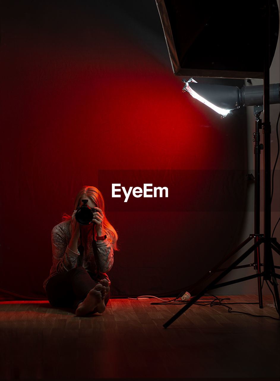 Woman sitting in a photo studio with a camera against a red light background