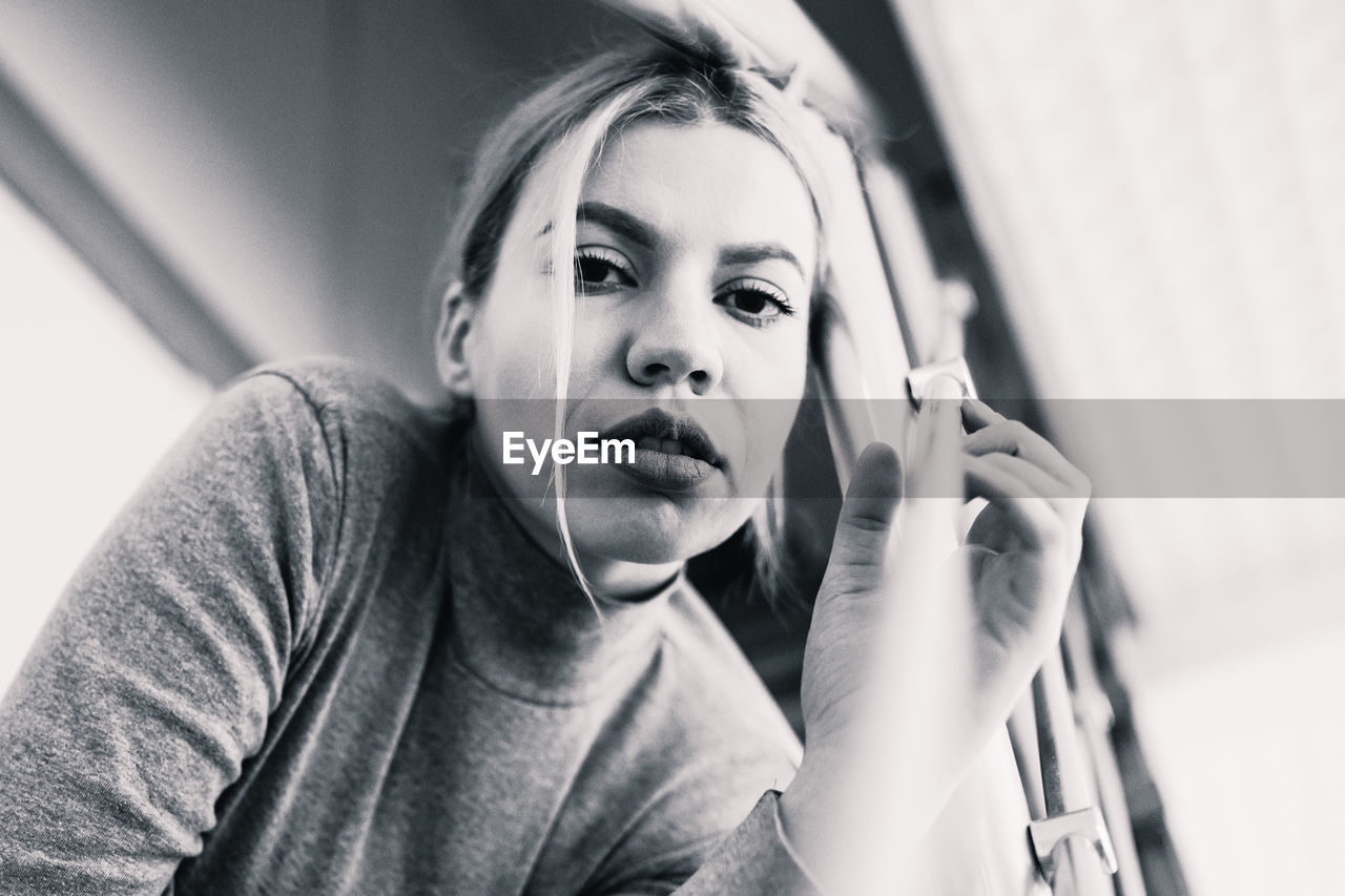 Low angle portrait of young woman sitting by railing at home