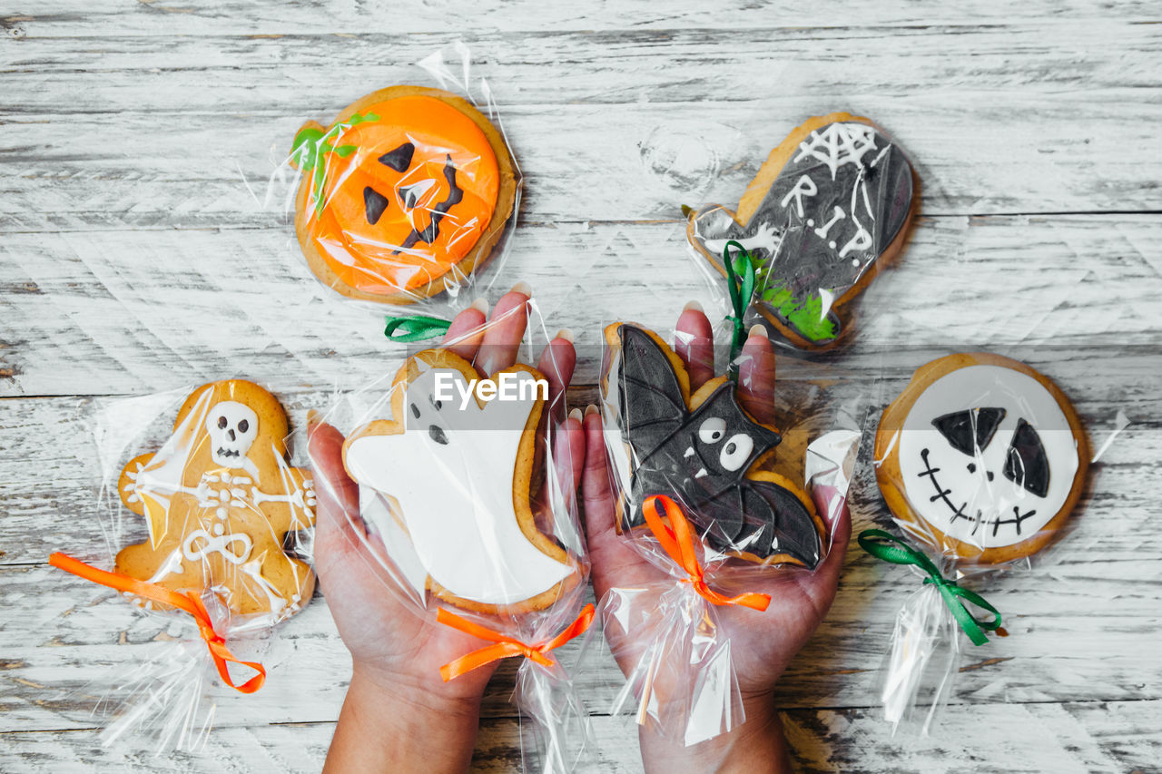 Cropped hands of woman holding various cookies wrapped in plastic over wooden table during halloween