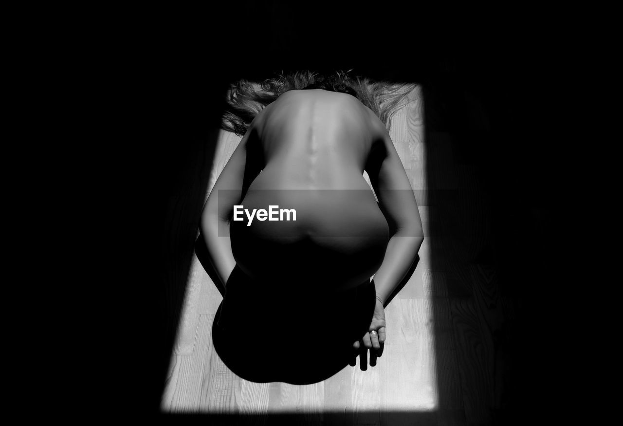 High angle view of depressed naked woman bending on floor in darkroom