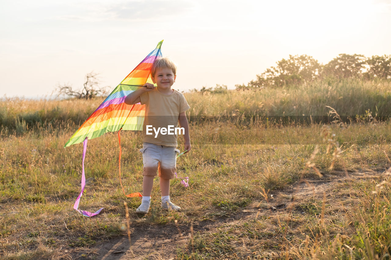 Happy little kid boy having fun with kite in nature at sunset