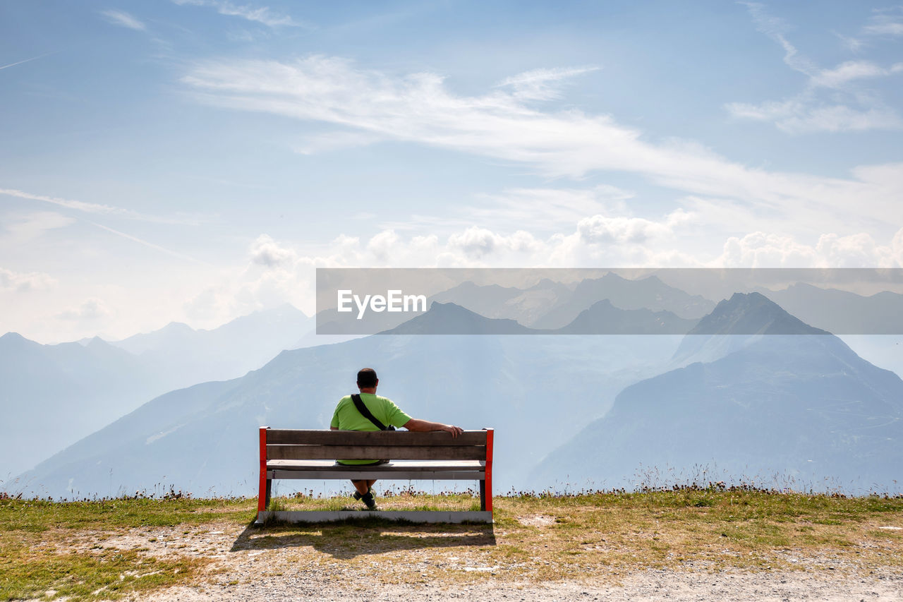 Rear view of man sitting on bench against mountains