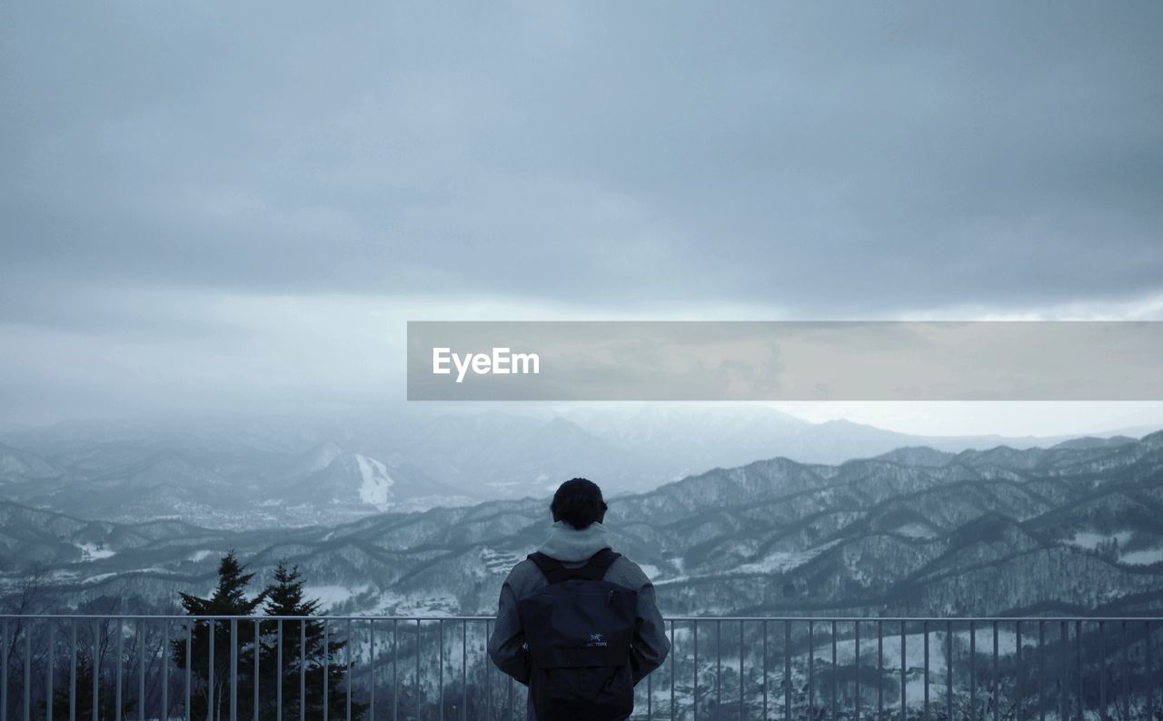 Person standing by railing at observation point against mountain range