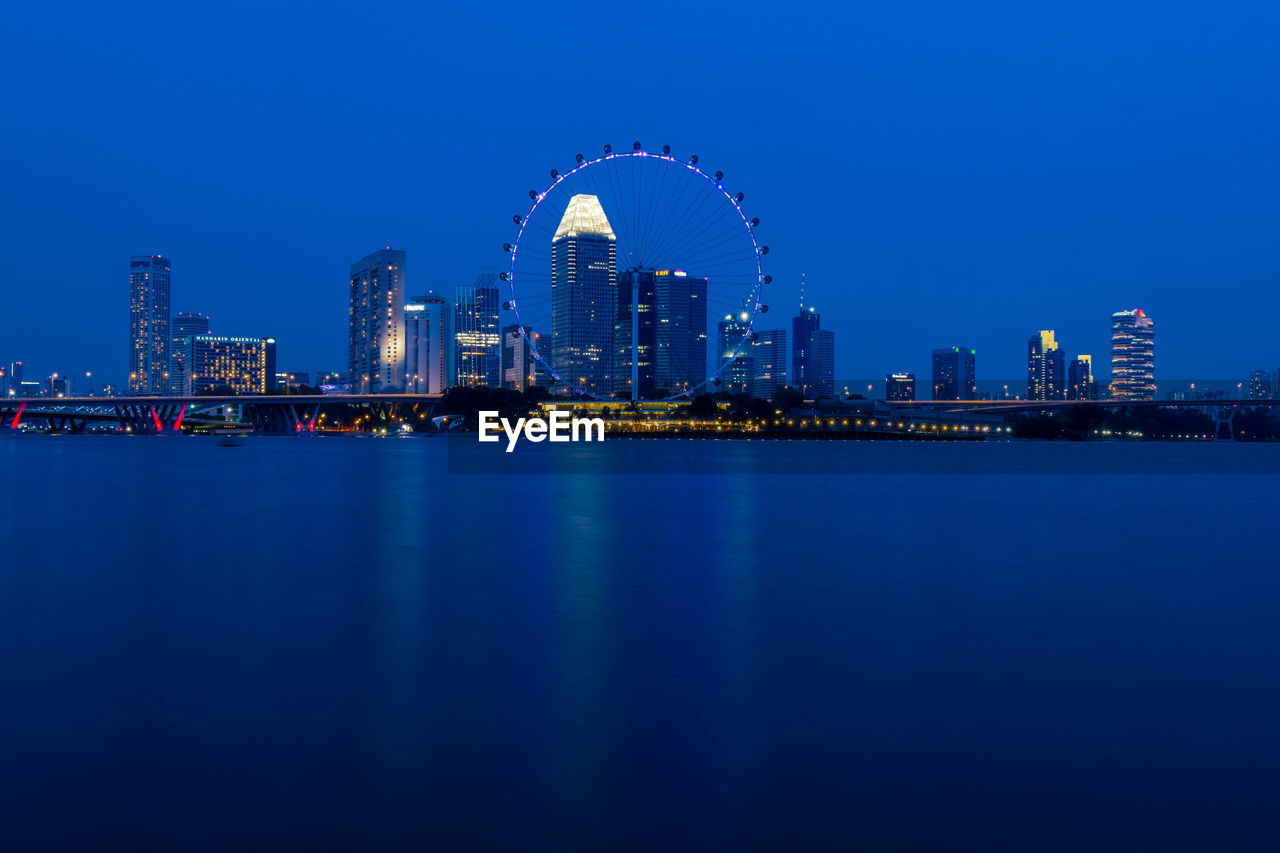 Singapore flyer by bay of water against clear blue sky in city