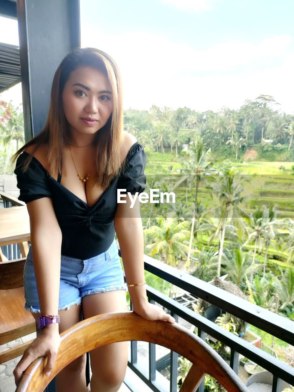 PORTRAIT OF BEAUTIFUL YOUNG WOMAN SITTING ON RAILING AGAINST BLURRED BACKGROUND