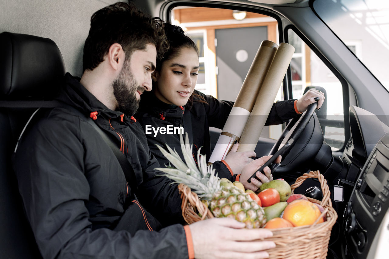 Young delivery man and woman with fruits and packages in truck