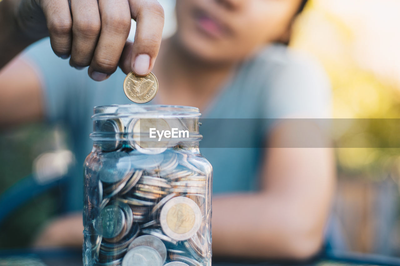 Close-up of woman putting coins in glass jar