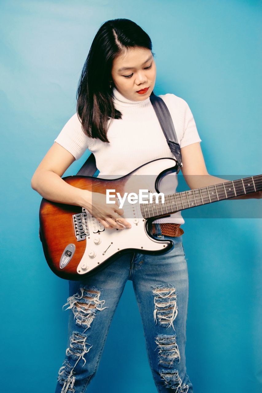 PORTRAIT OF YOUNG WOMAN PLAYING GUITAR