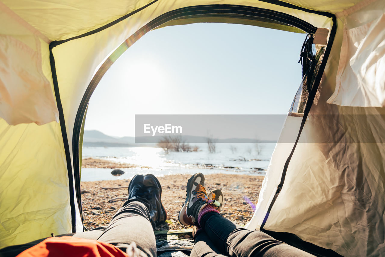 Pov view from camping tent of couple of hikers lying at campsite on sunny day near pond in mountains